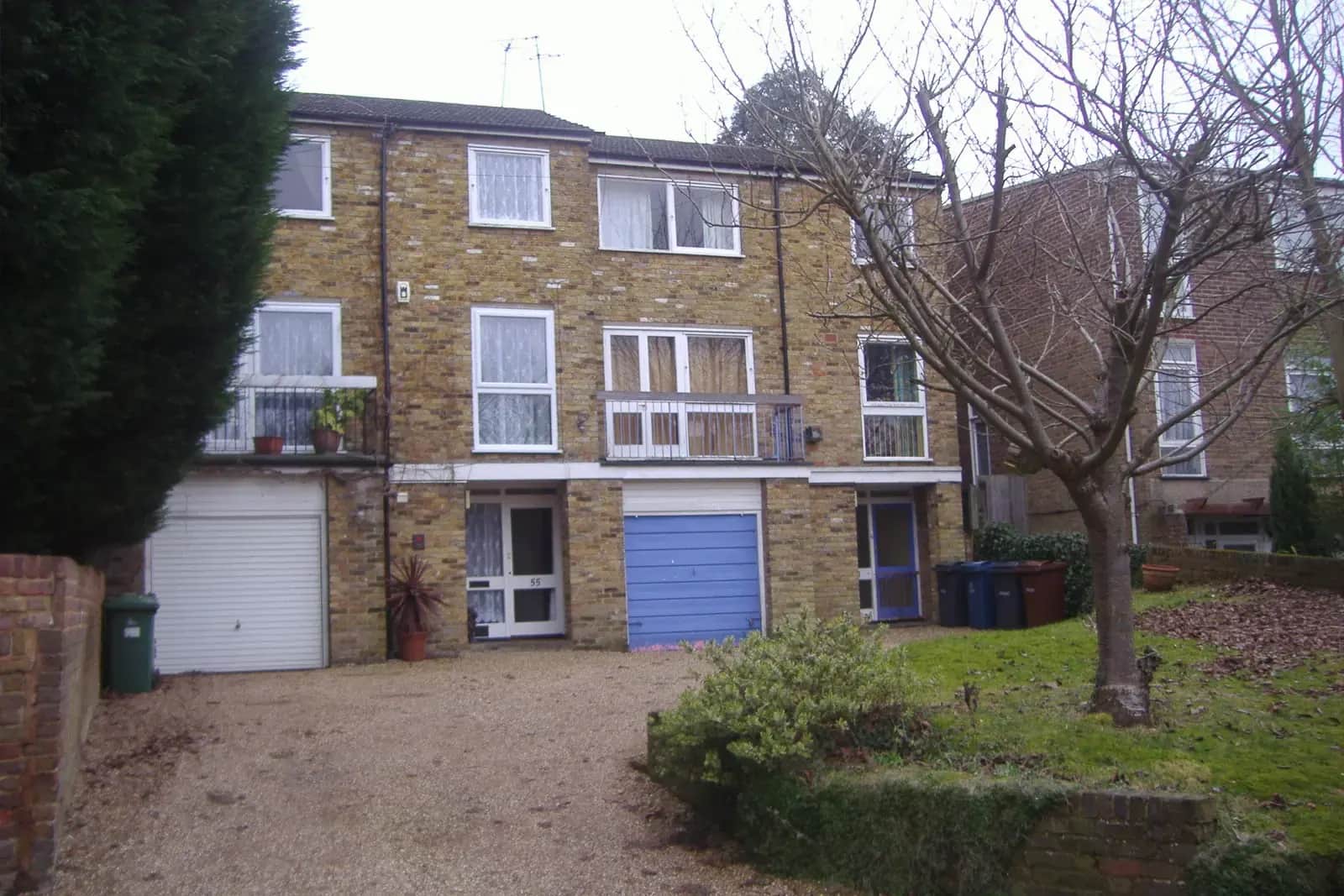 Brick townhouse with two integral garage doors, one white and one blue, on a gravel drive