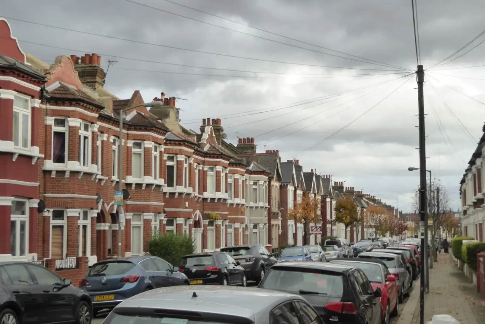 A long terrace of red-brick Victorian houses with bay windows and roof dormers on Gaskarth Road, parked cars along one side and overhead cables