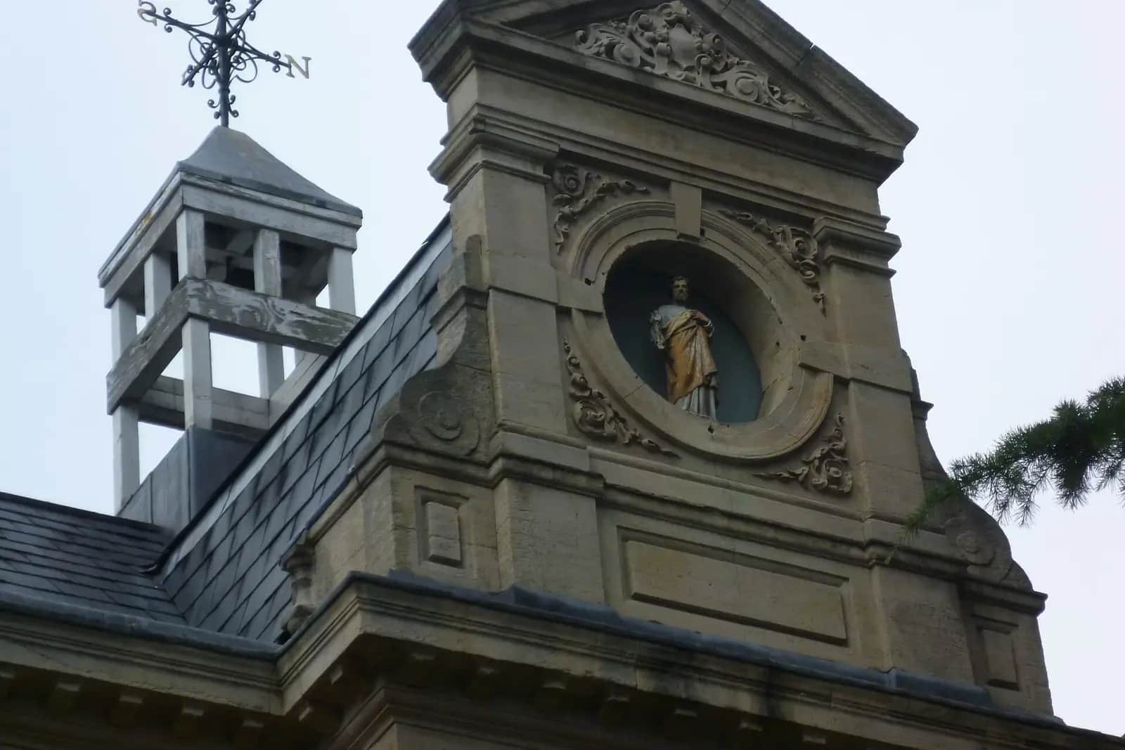 The stone gable of a former council office with a bell turret, a carved round niche holding a statue and ornate scrollwork, against a pale sky