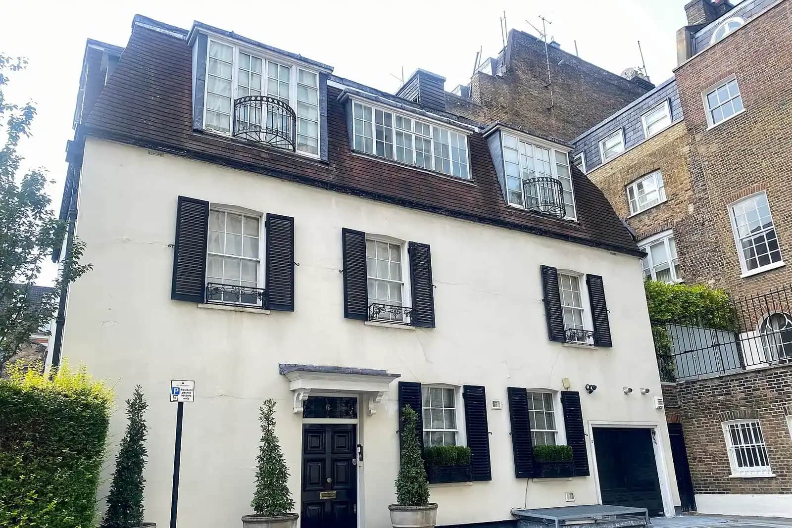 White painted three-storey mews house with black shutters, a mansard roof with dormers and a black front door beside its garage