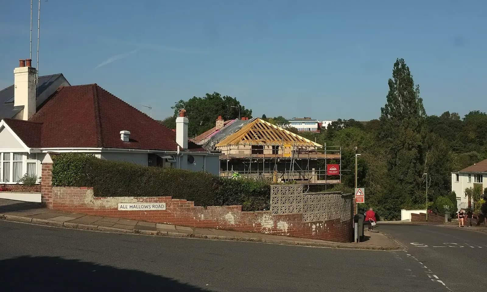 New timber roof frame on a house extension behind a hedge and brick wall on All Hallows Road, scaffolding around the new structure