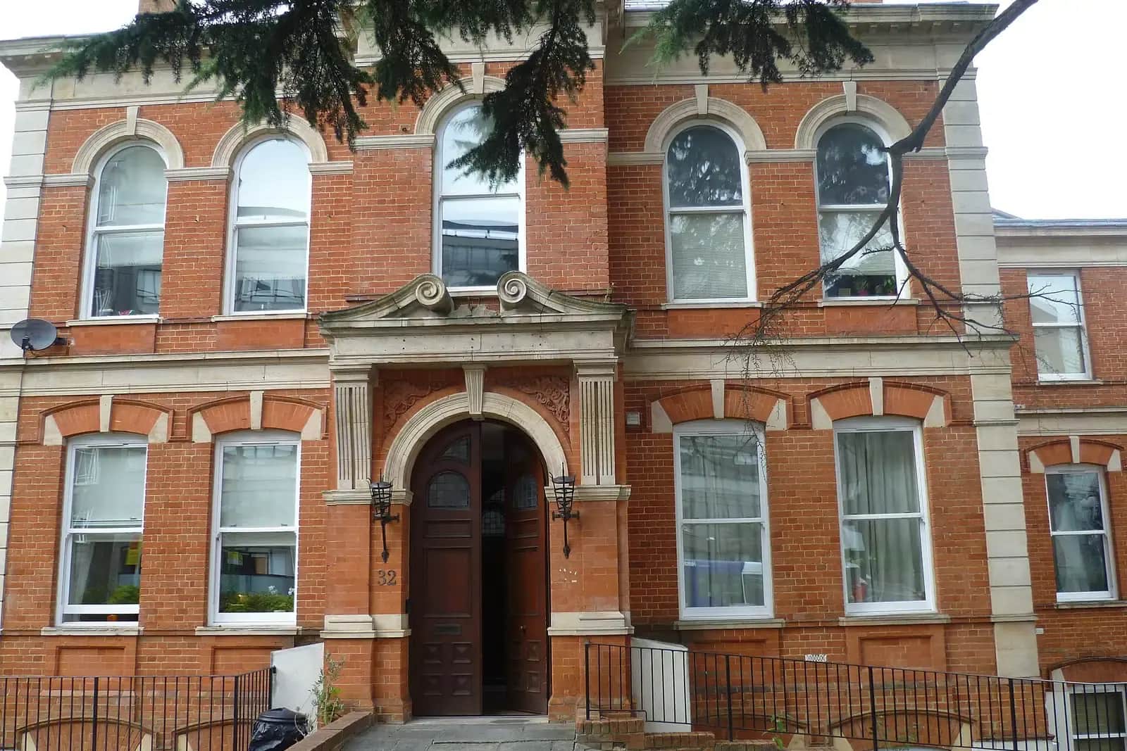 Entrance of a red-brick Victorian building with a stone porch, an arched dark wooden door and arched windows