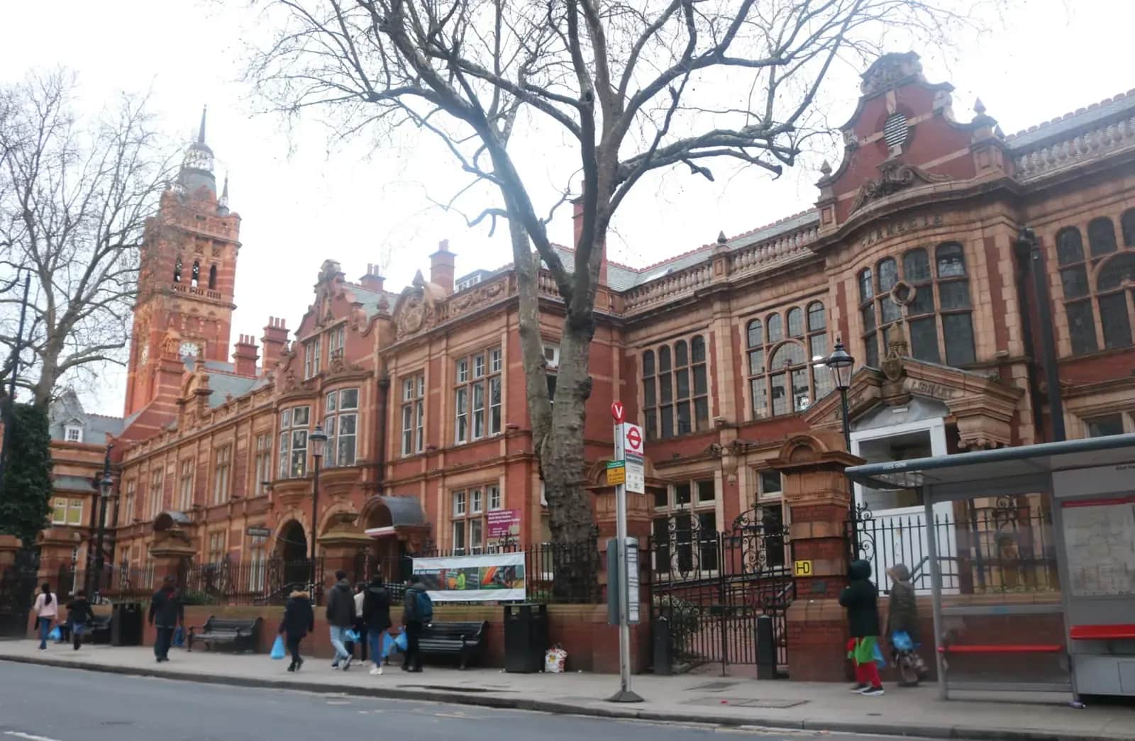 Red-brick and terracotta East Ham Town Hall with a clock tower, a bus shelter and pedestrians in front