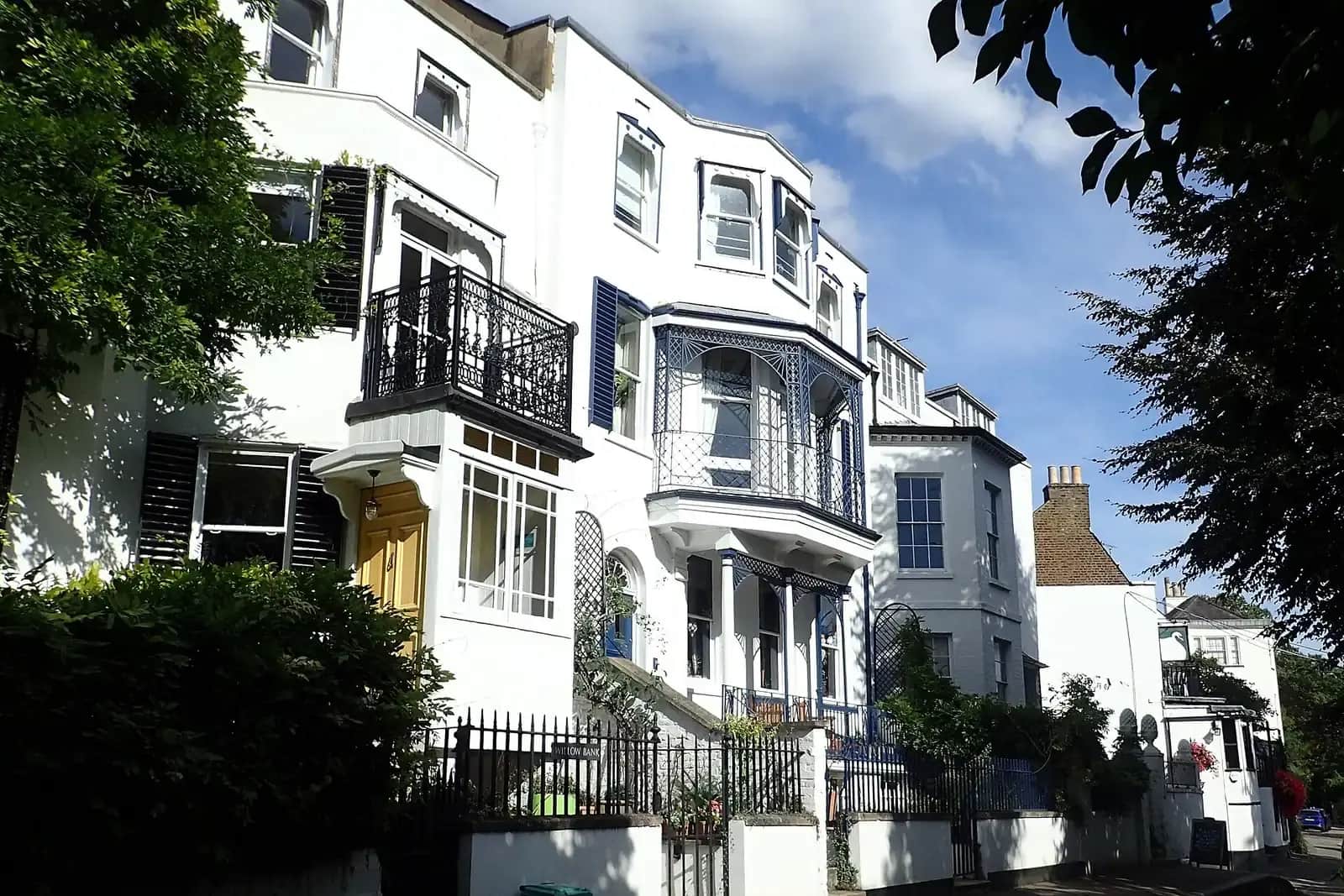 Cream and white houses at Twickenham Riverside with iron balconies, a blue lattice veranda and sunlit trees