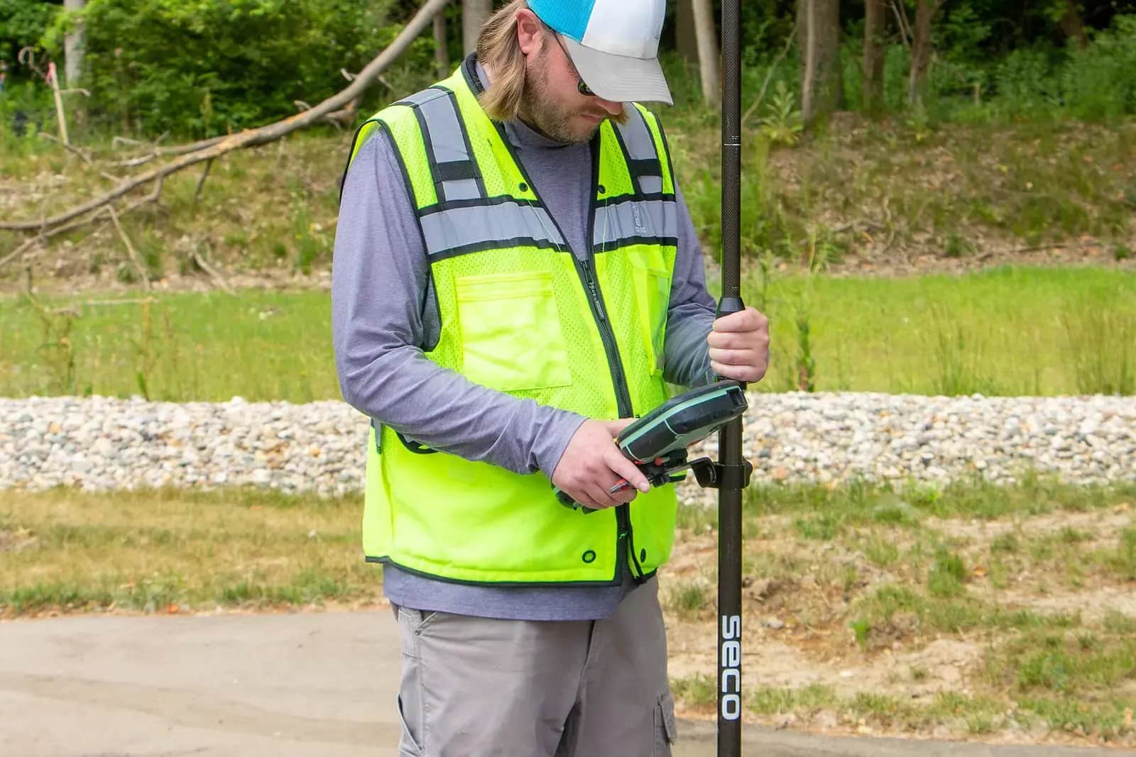 Surveyor in hi-visibility vest and cap holding a GNSS receiver pole and a handheld controller