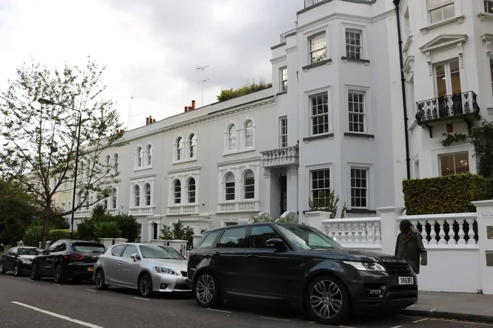 White stuccoed Victorian terrace on Kensington Park Road in Notting Hill with a balustraded porch, parked cars and a tree