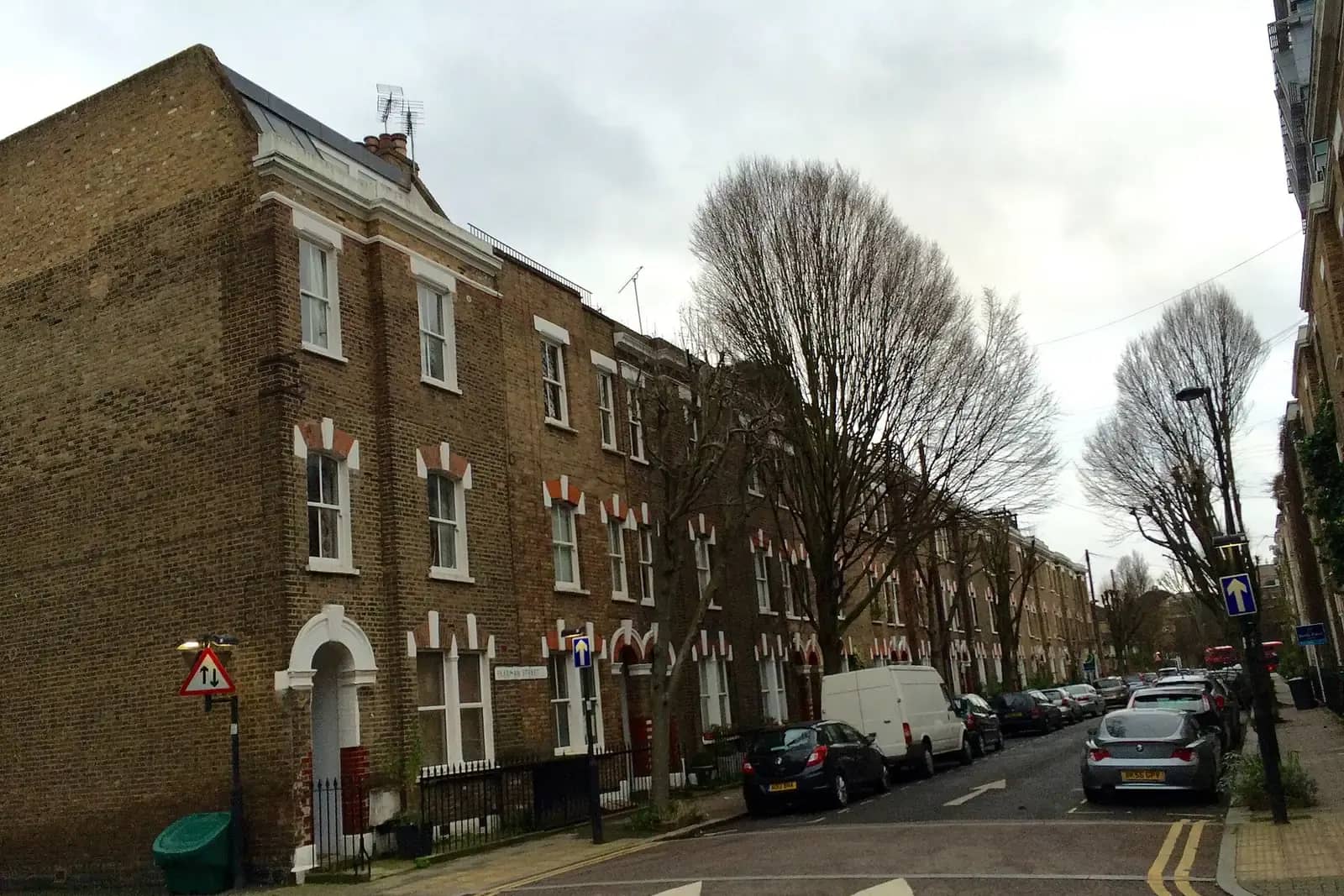 Corner of yellow-brick Victorian terraced houses with red brick arches on Pearman Street in Lambeth, a white van and plane trees