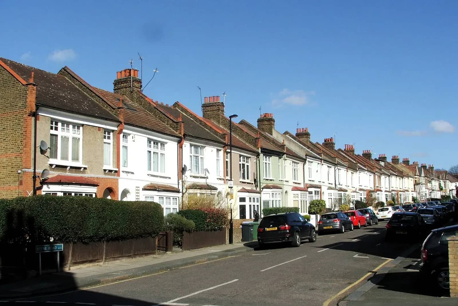 Terrace of Edwardian houses on Boyne Road in Lewisham with painted brick fronts and hedged front gardens under a blue sky