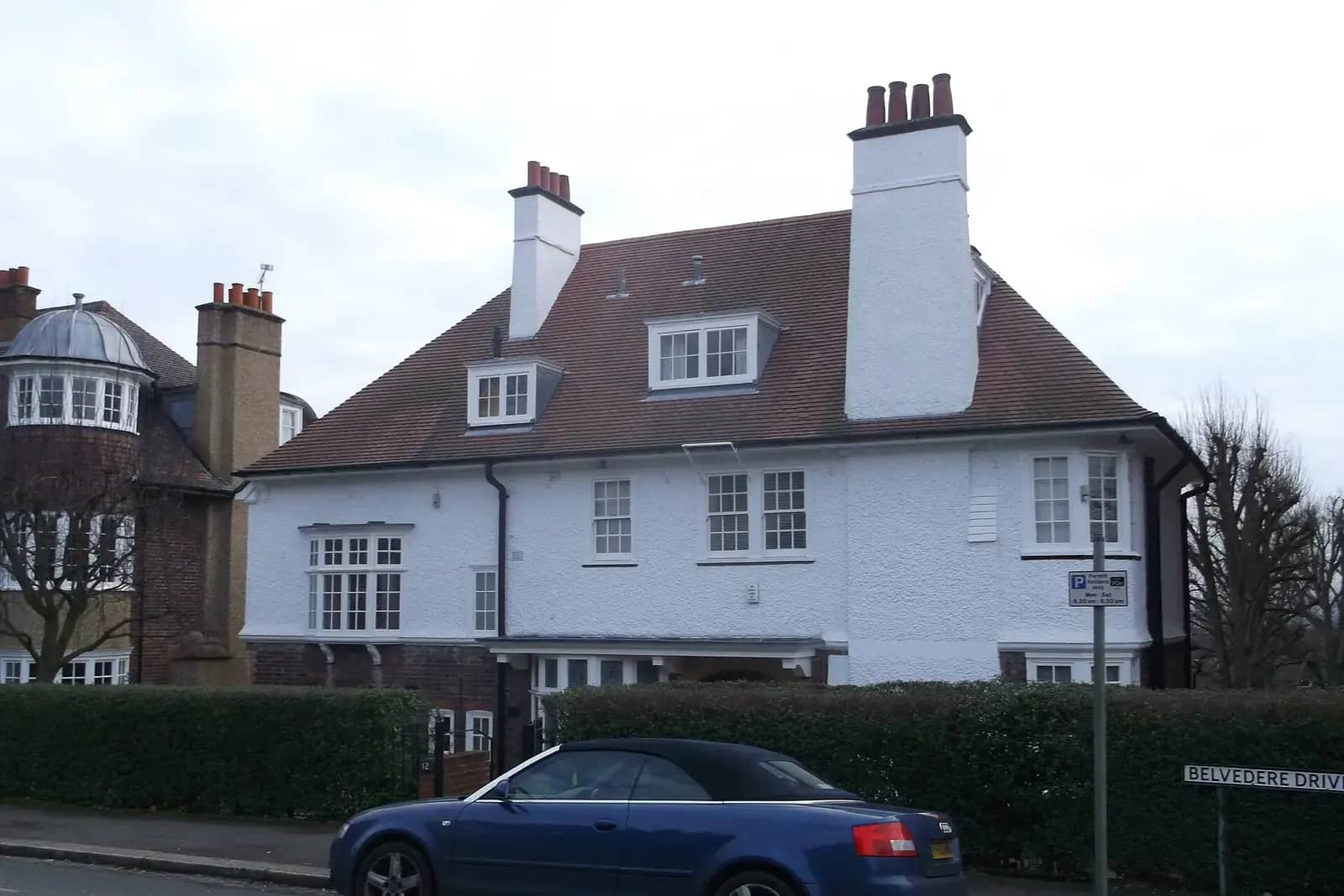 Large white roughcast house with dormer windows and tall chimneys on Belvedere Drive in Wimbledon, a blue convertible in front