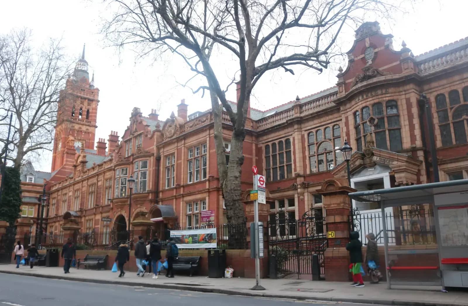 Red-brick and terracotta East Ham Town Hall with a clock tower, a bus shelter and pedestrians in front