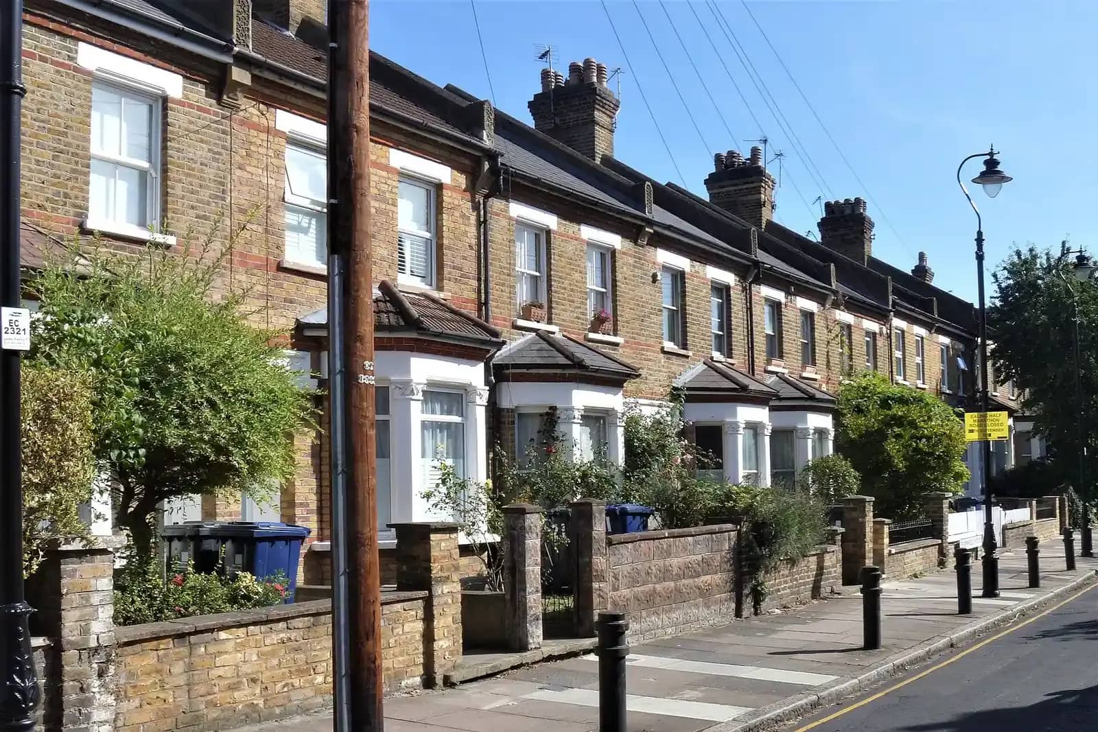 A terrace of London stock brick houses with white bay windows and low front walls along a street in Ealing, a telegraph pole in the foreground