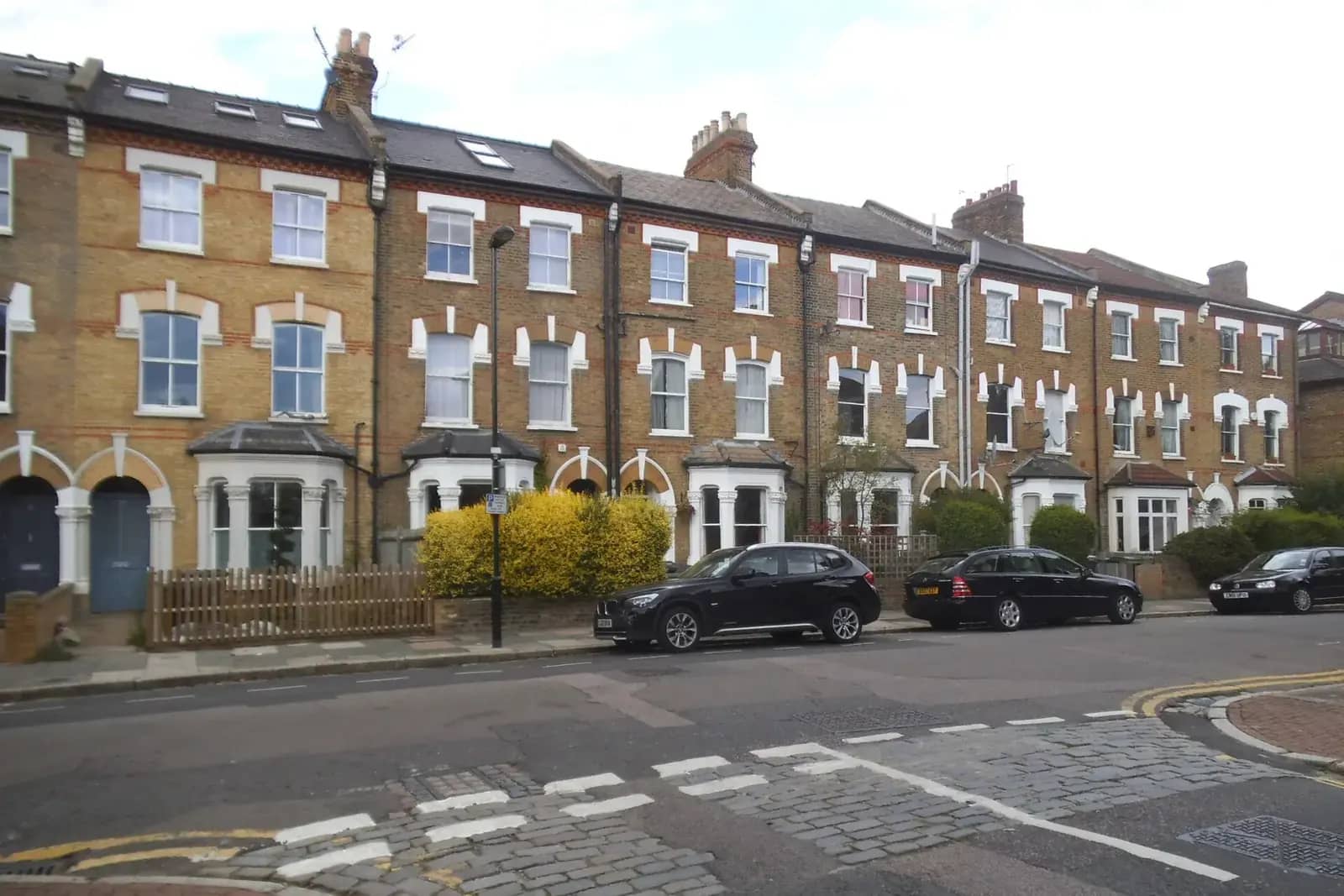 A terrace of yellow-brick Victorian houses with white bay windows and roof windows on Palace Road in Crouch End, a black estate car parked in front