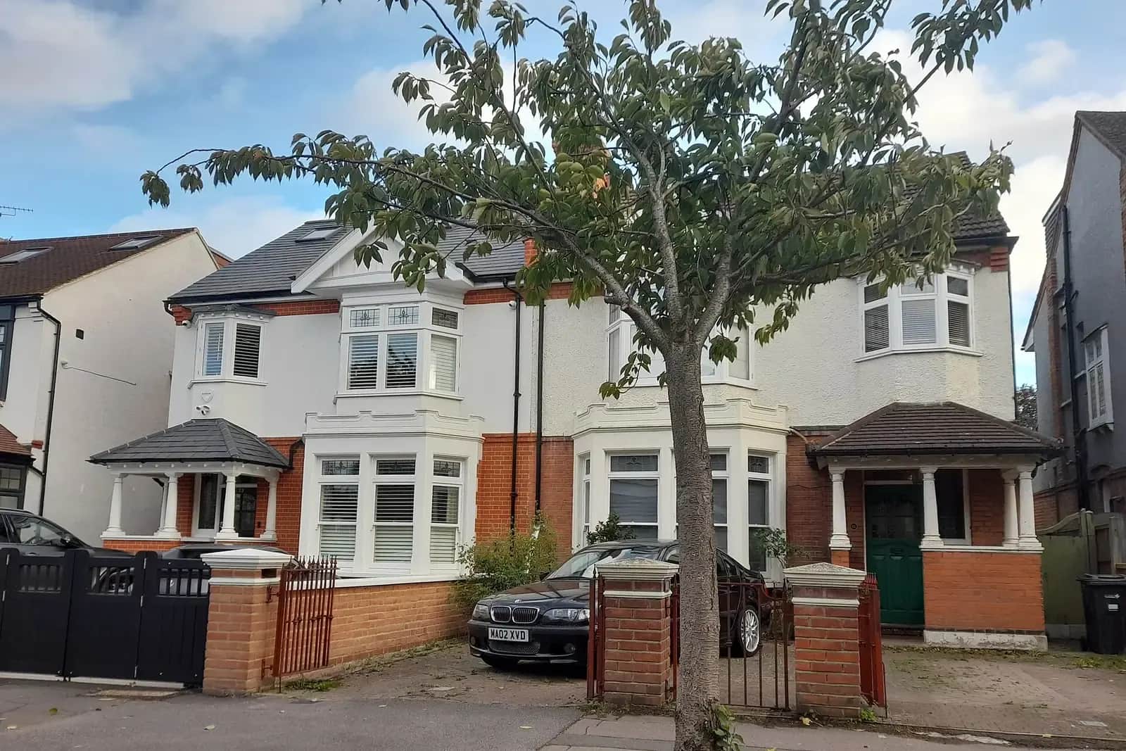 A pair of Edwardian semi-detached houses on Redbridge Lane West in Wanstead with white bay windows, red brick, a loft conversion and a car on the drive
