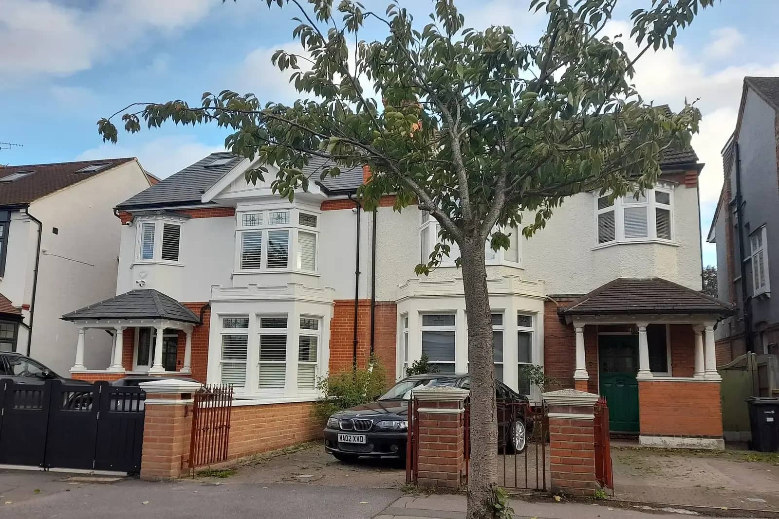A pair of Edwardian semi-detached houses on Redbridge Lane West in Wanstead with white bay windows, red brick, a loft conversion and a car on the drive