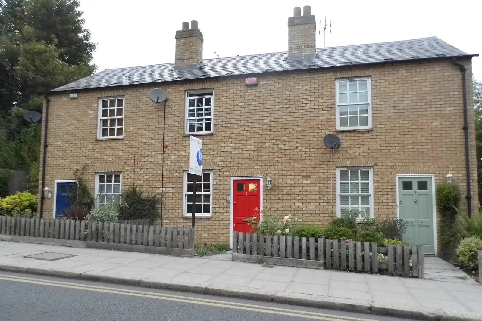 Pair of yellow-brick cottages on Windmill Hill in Enfield with one red and one green front door behind a low picket fence