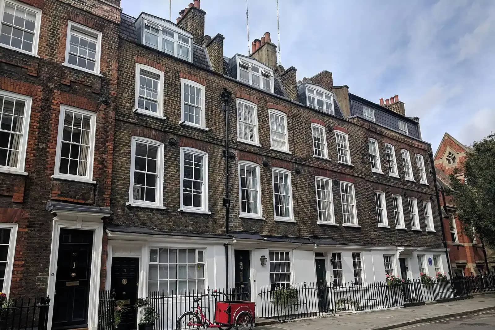 Georgian terrace of dark brick houses with white sash windows, black railings and roof dormers, a red cargo bike parked outside