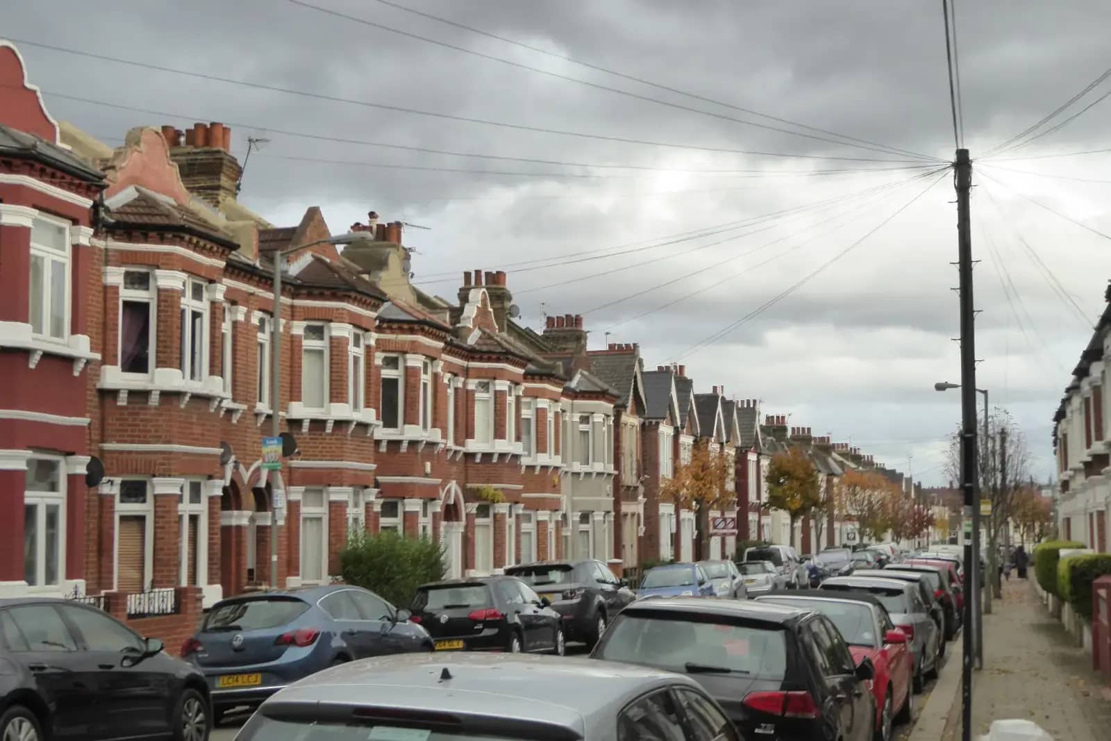 A long terrace of red-brick Victorian houses with bay windows and roof dormers on Gaskarth Road, parked cars along one side and overhead cables