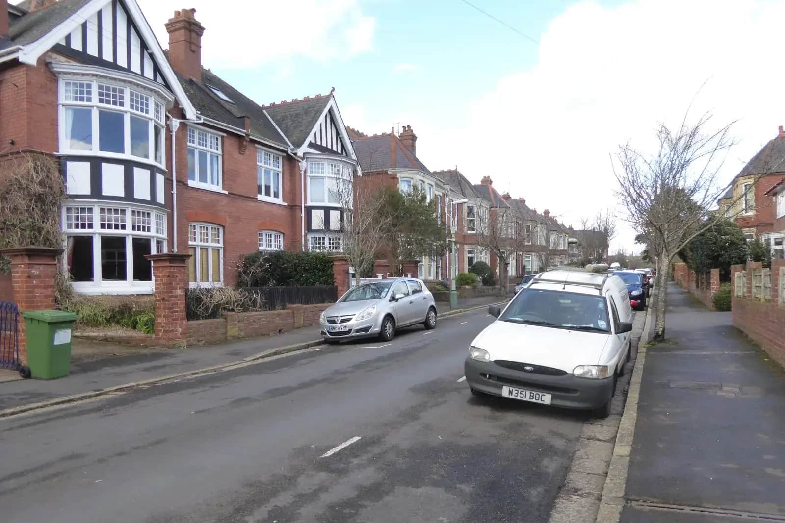 A street of red-brick Edwardian houses with white bay windows, one with a roof window, on Marlborough Road in Exeter, a white van parked on the right