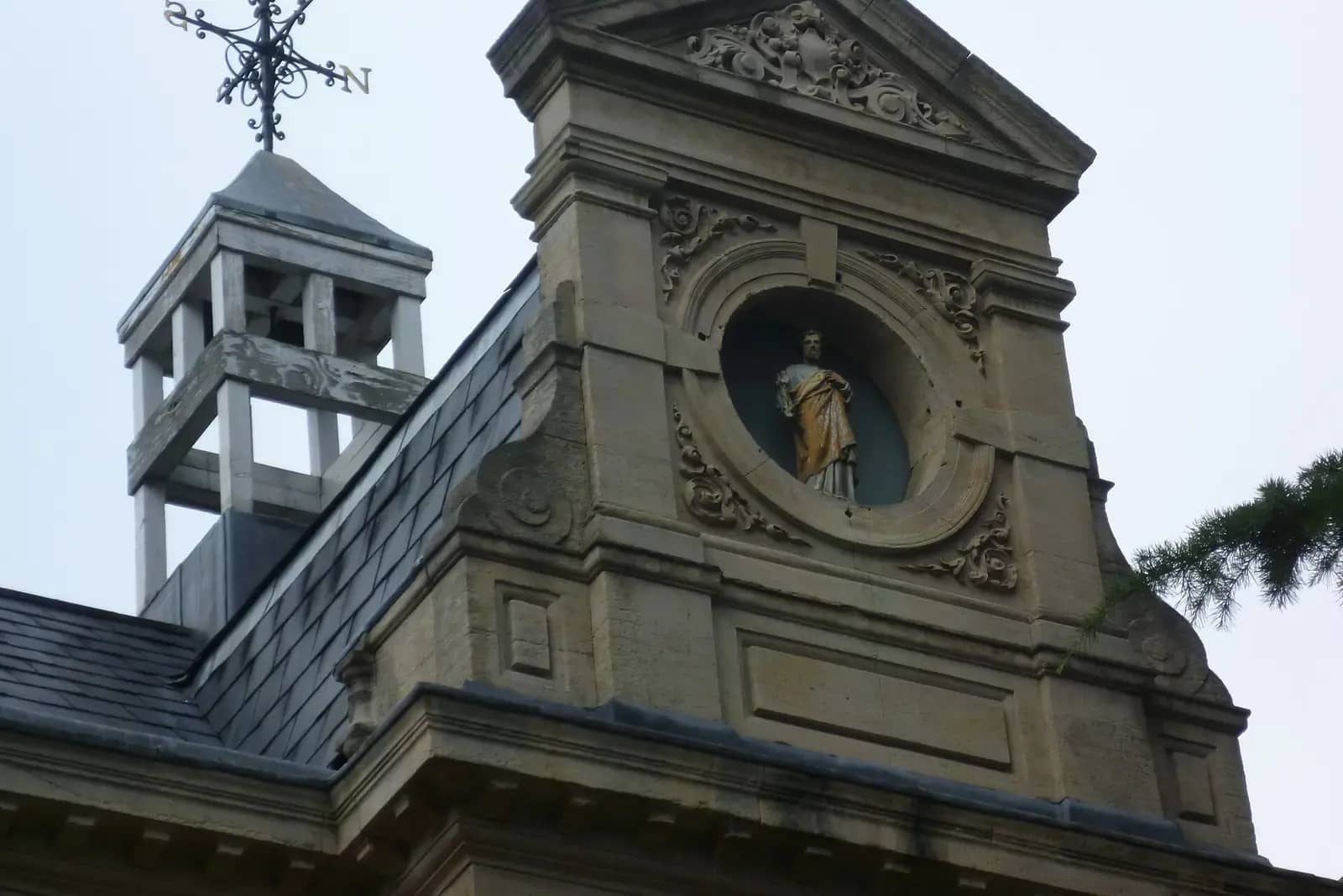 The stone gable of a former council office with a bell turret, a carved round niche holding a statue and ornate scrollwork, against a pale sky