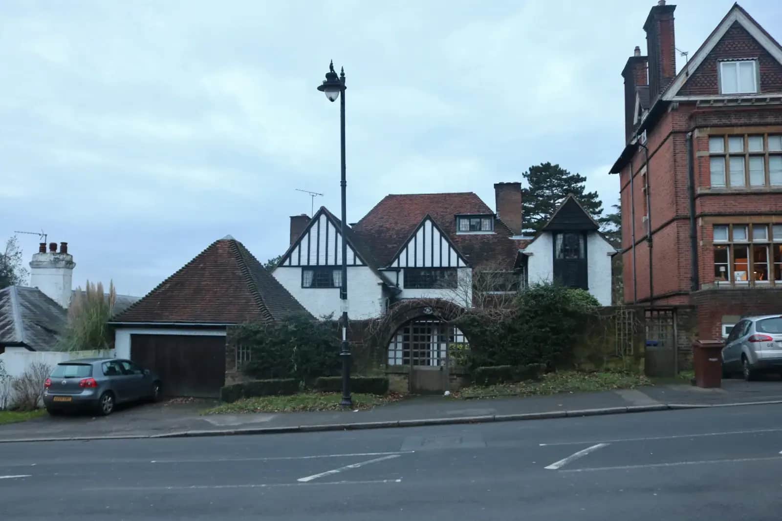 Mock-Tudor detached house on Sudbury Hill in Harrow with a black lamp post, a hipped garage and a red-brick house beside it