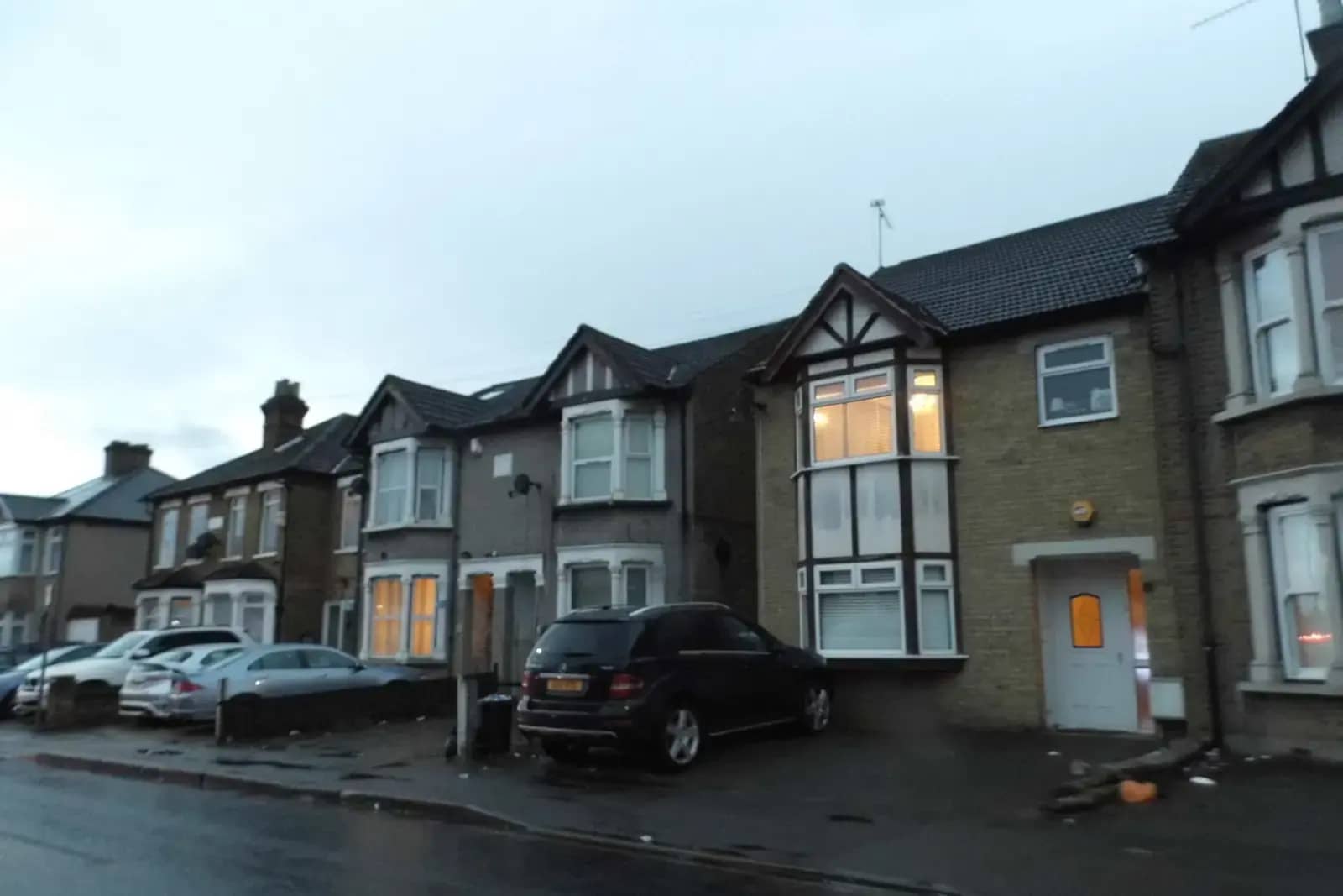 Houses on Havering Road in Collier Row, one with a modern brick side extension with large windows, parked cars on a wet evening