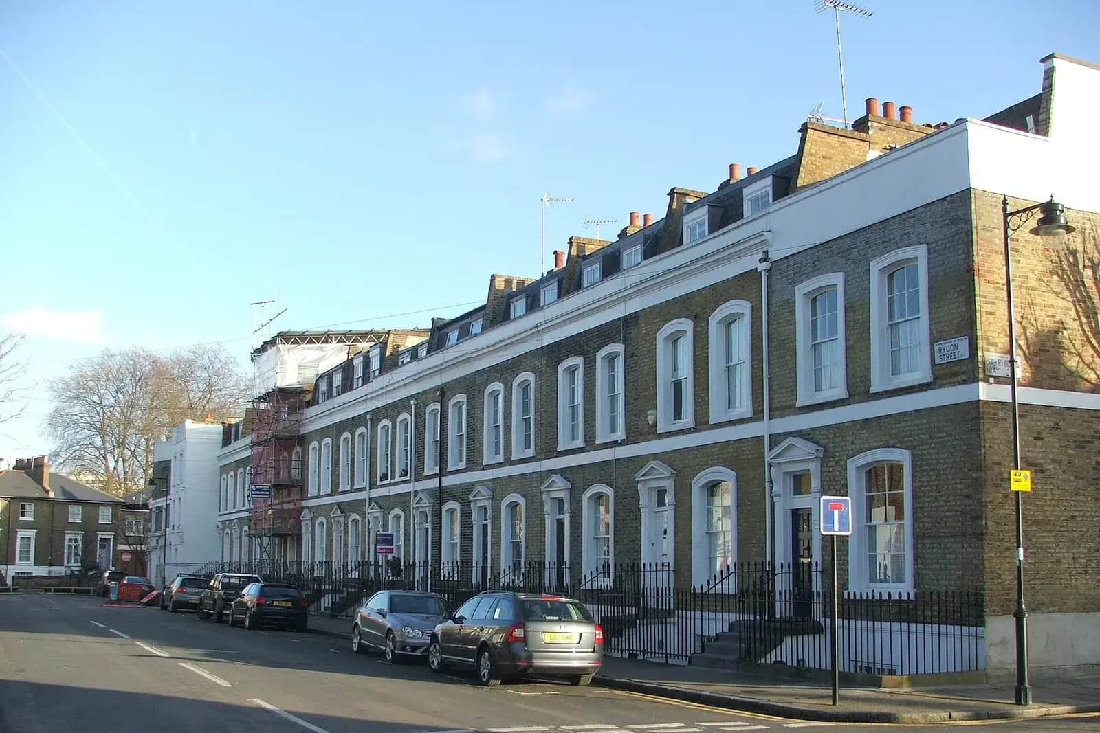Curving terrace of yellow-brick houses on Rydon Street in Islington with white window frames, a lamp post and parked cars