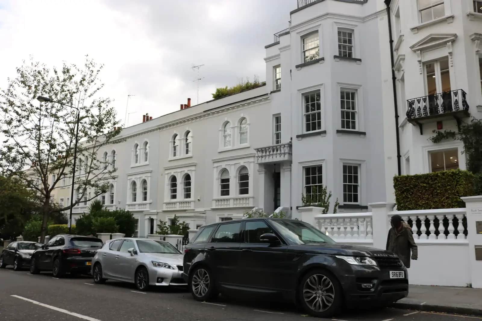 White stuccoed Victorian terrace on Kensington Park Road in Notting Hill with a balustraded porch, parked cars and a tree