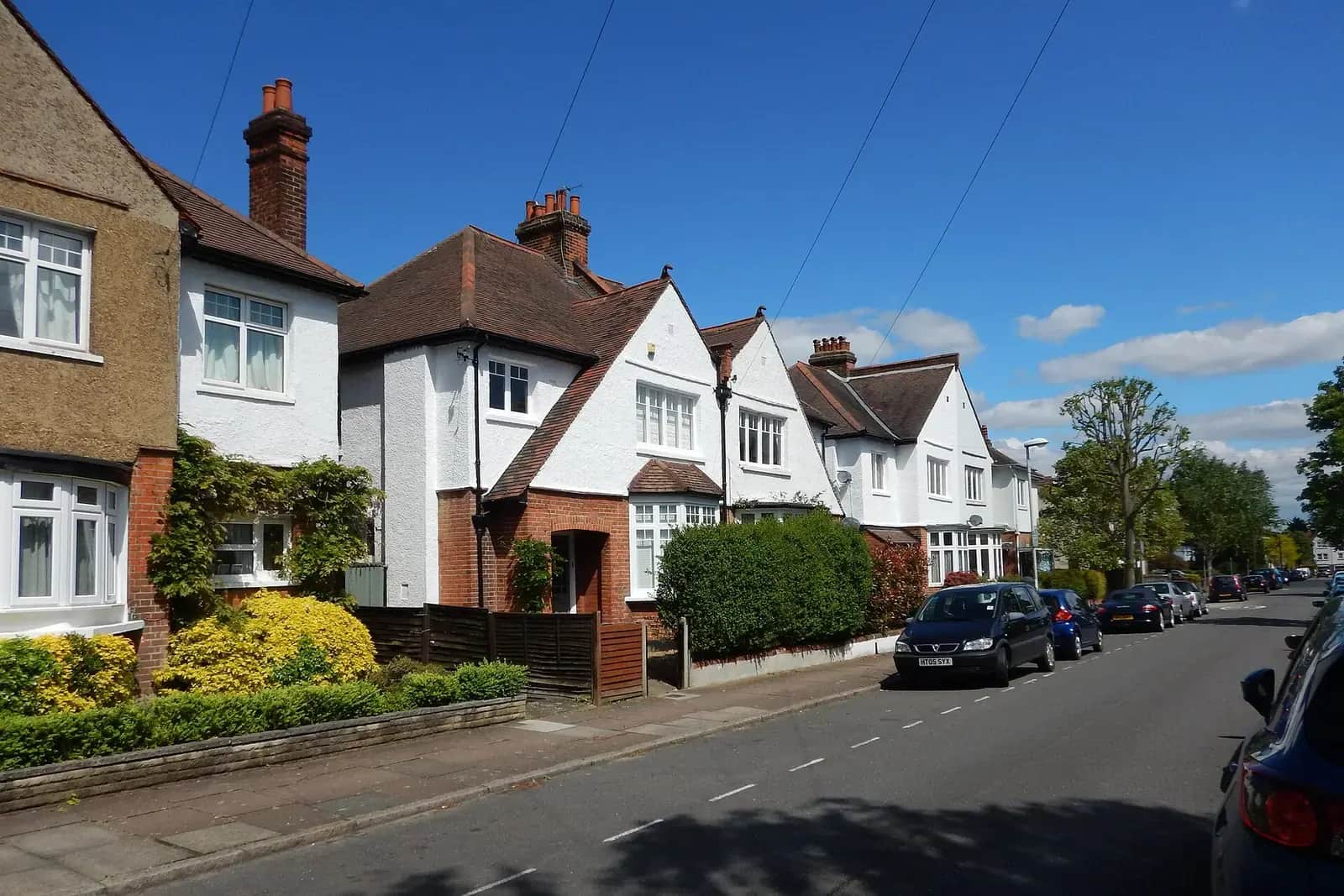 Roughcast Edwardian houses with gables and bay windows on Guildford Avenue in Surbiton, a dark car parked under a blue sky