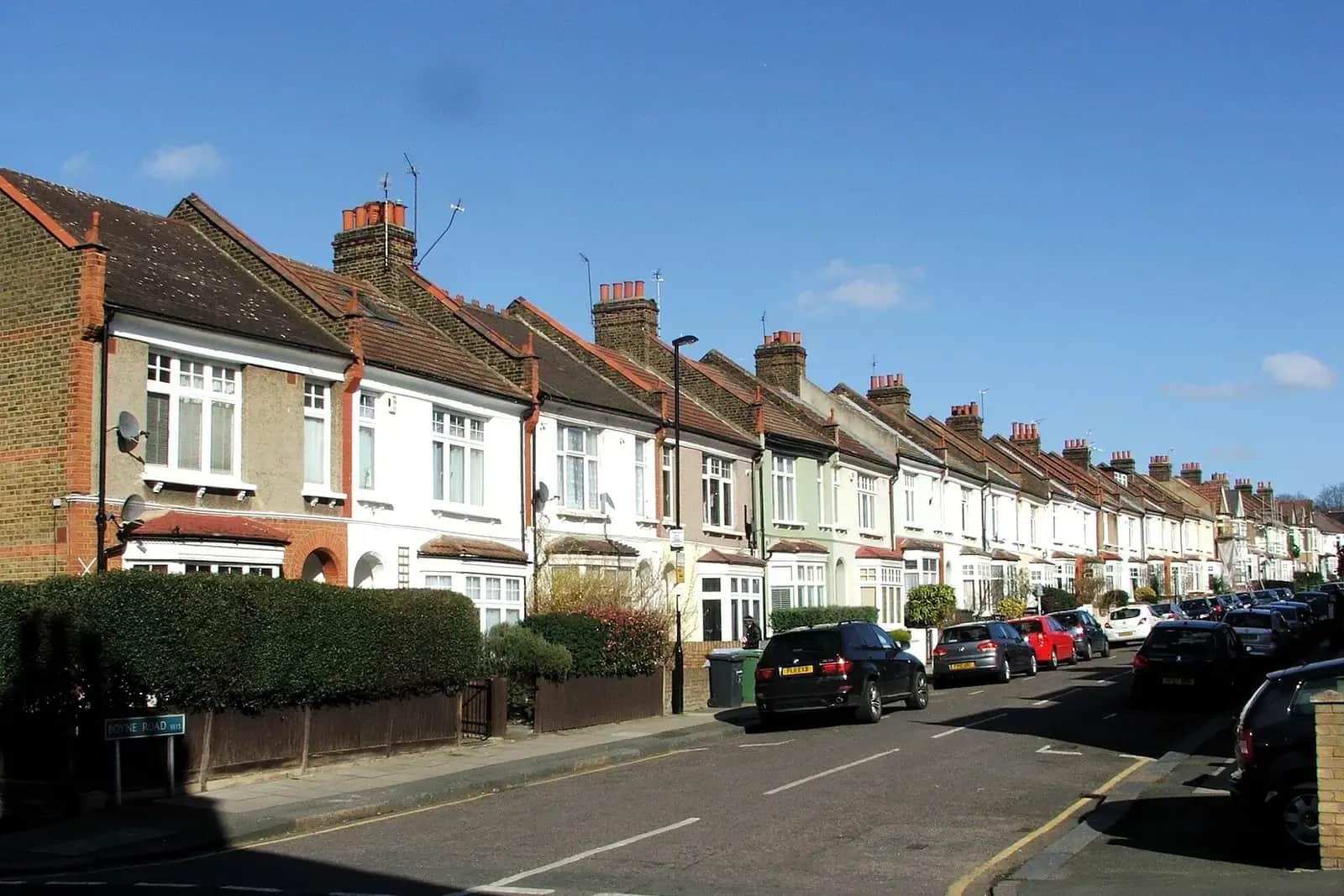 Terrace of Edwardian houses on Boyne Road in Lewisham with painted brick fronts and hedged front gardens under a blue sky