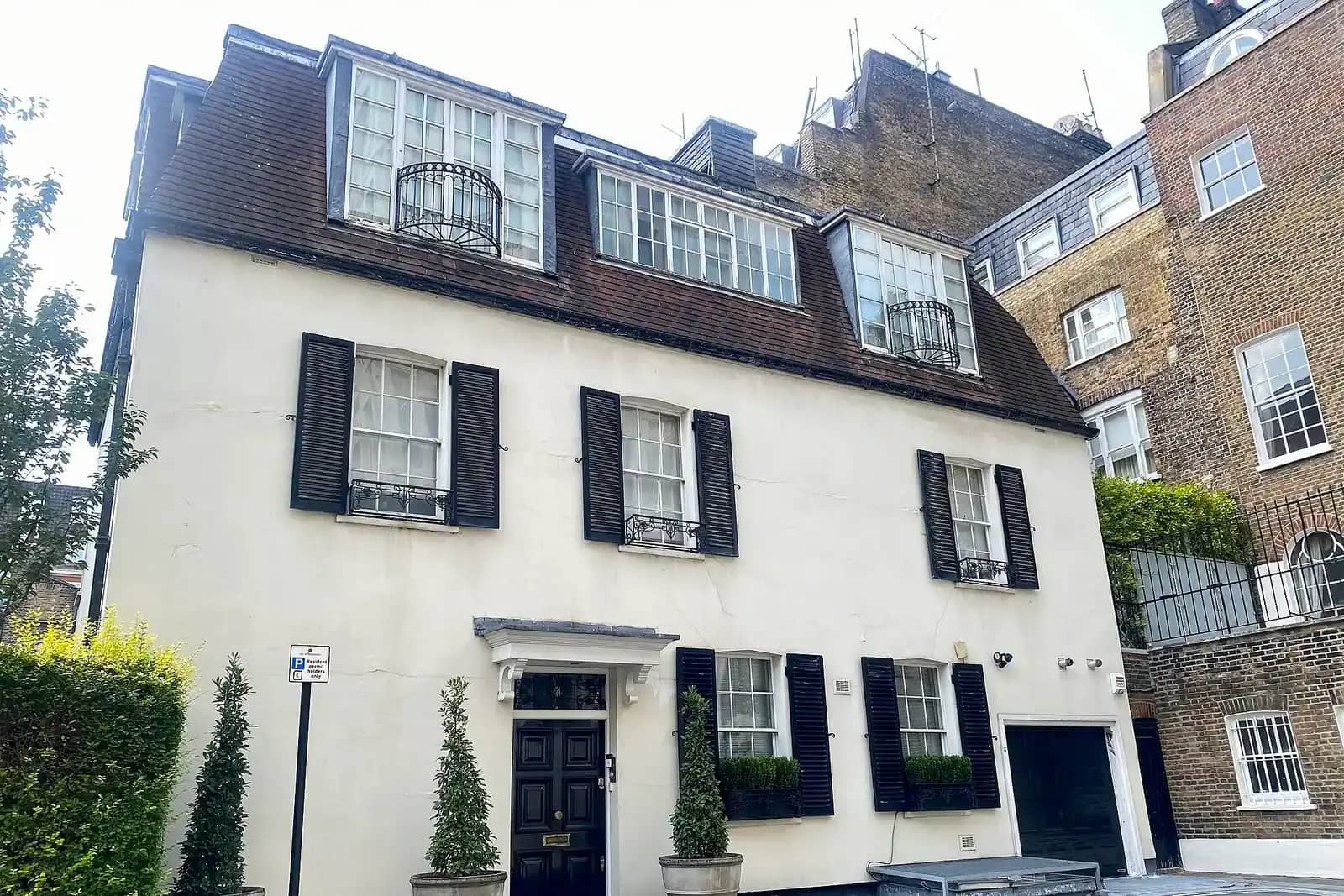 White painted three-storey mews house with black shutters, a mansard roof with dormers and a black front door beside its garage