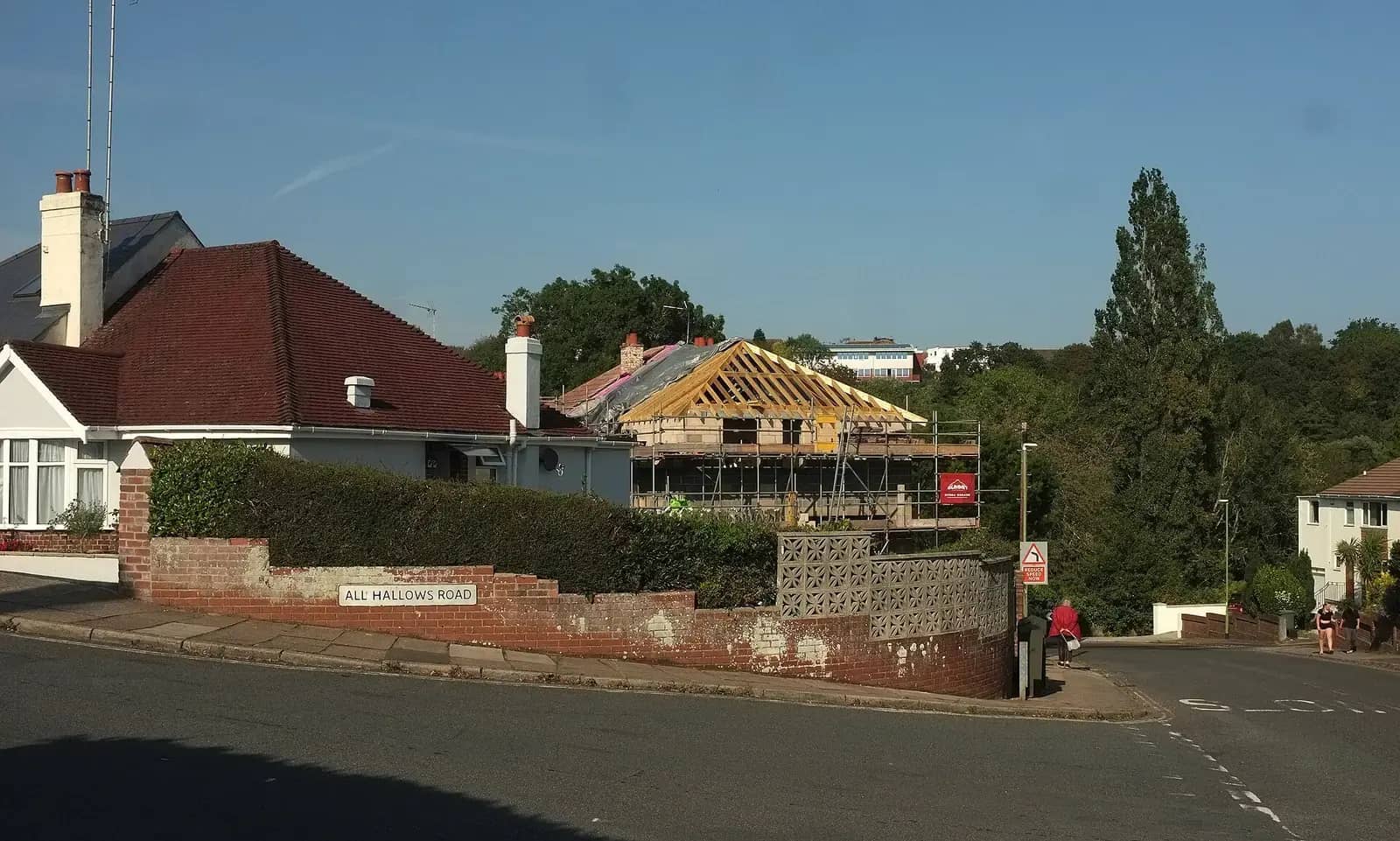 New timber roof frame on a house extension behind a hedge and brick wall on All Hallows Road, scaffolding around the new structure