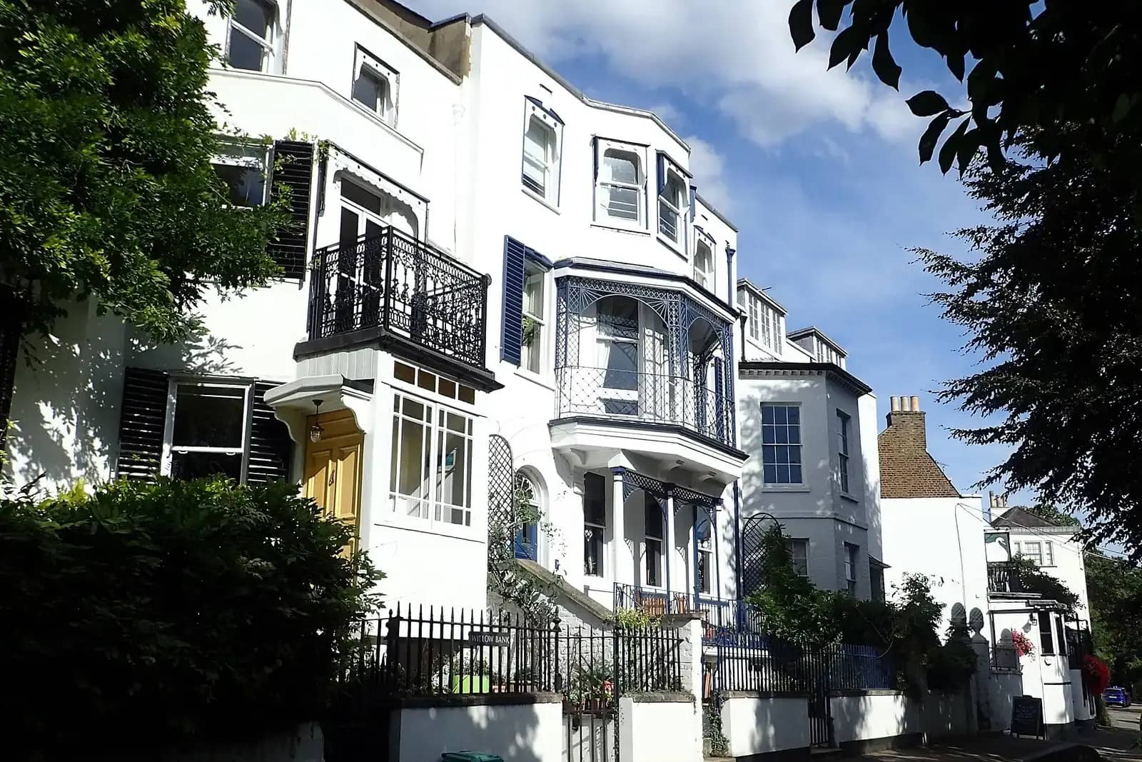 Cream and white houses at Twickenham Riverside with iron balconies, a blue lattice veranda and sunlit trees