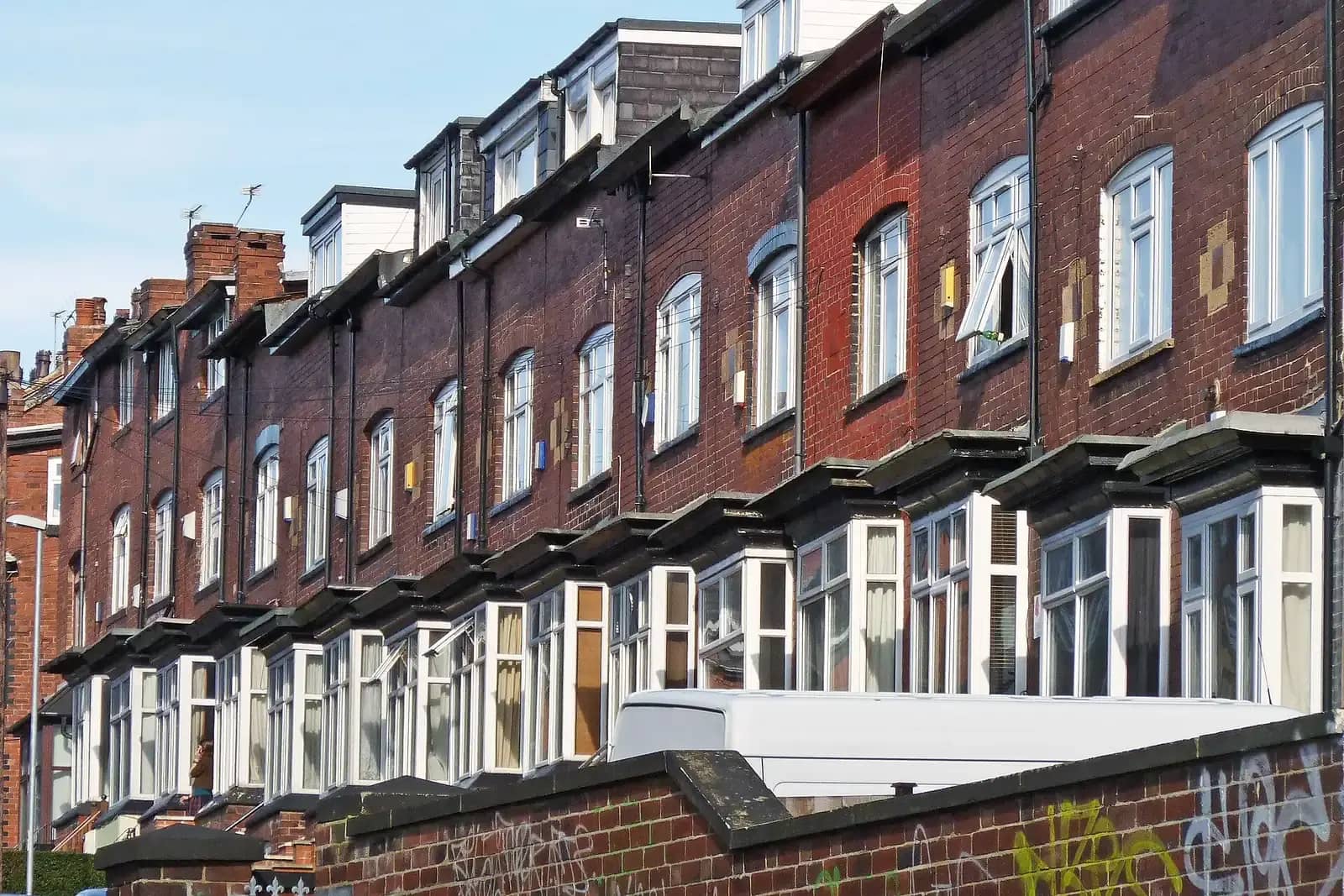 Long terrace of dark red brick houses with flat-roofed bay windows and roof dormers, climbing a hill, a white van parked in front