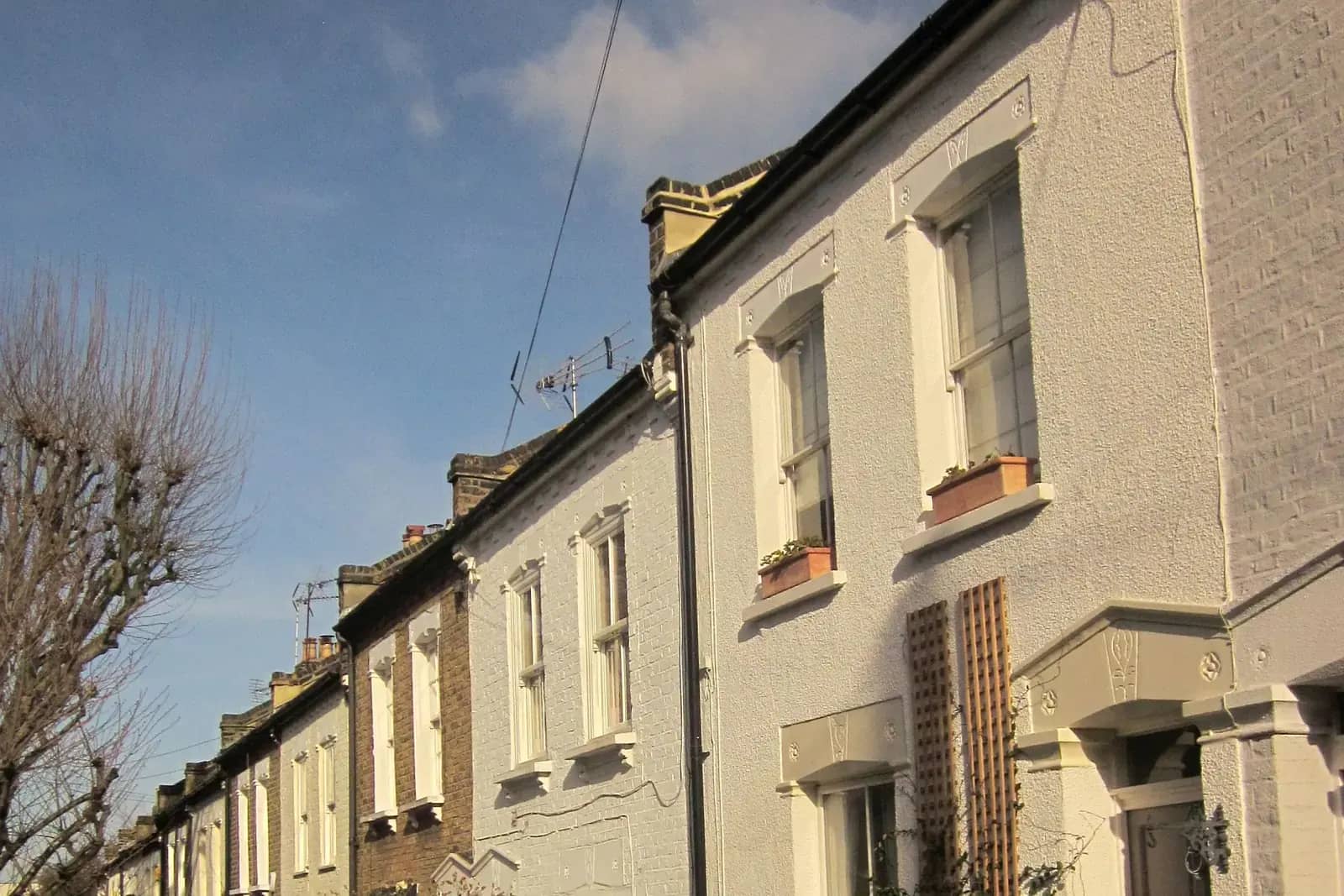 A terrace of white rendered Victorian houses with sash windows, flower boxes and wooden trellis, seen from the street at a low angle
