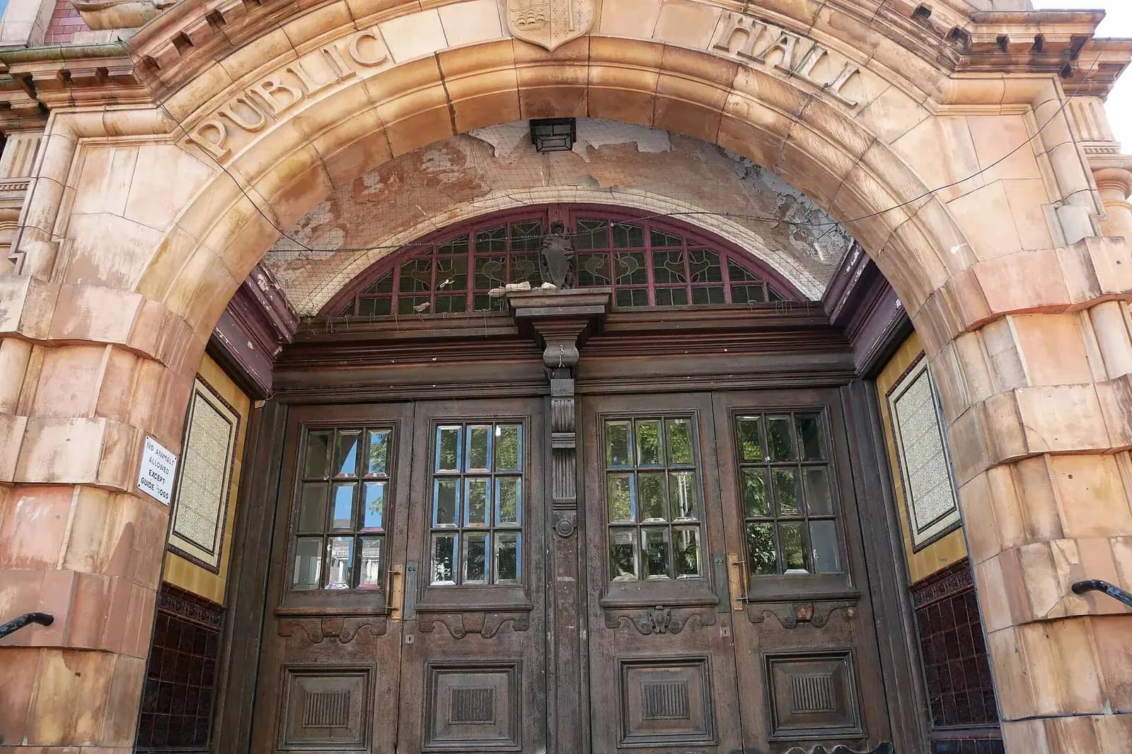 A carved terracotta arch over a pair of old wooden double doors with the words PUBLIC HALL above, on a Victorian public building