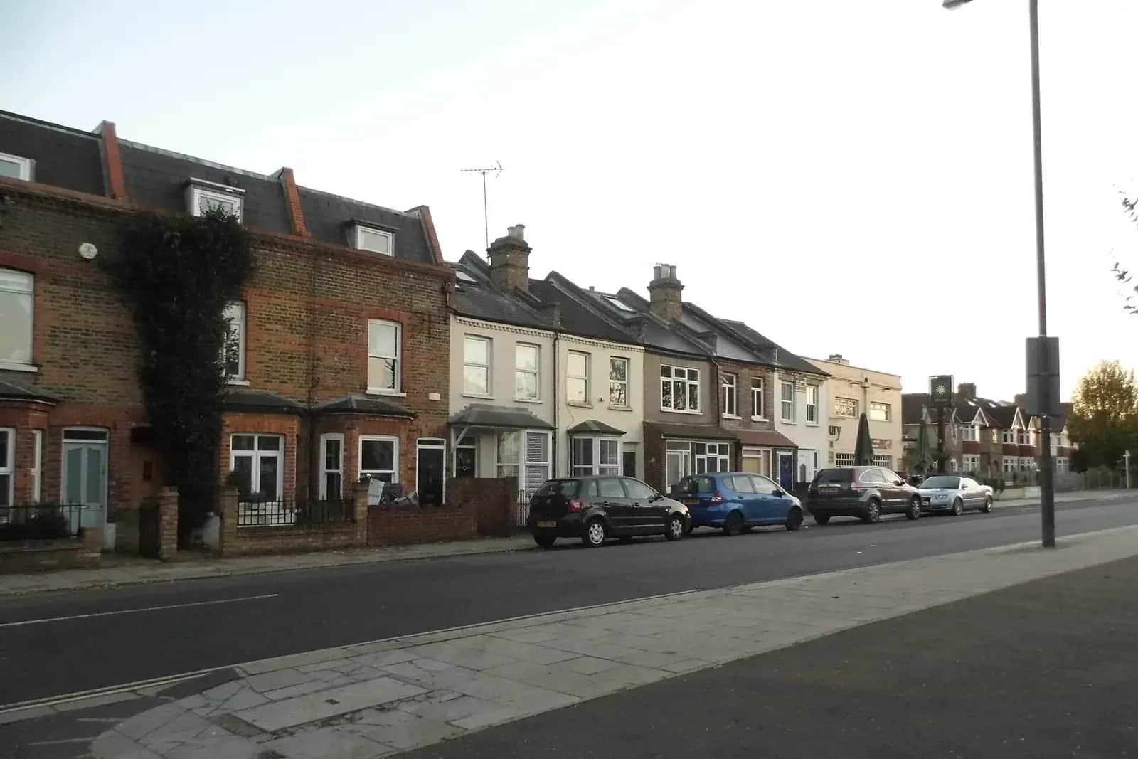 Row of brick terraced houses on Staines Road in Twickenham, some with roof windows, parked cars at the kerb