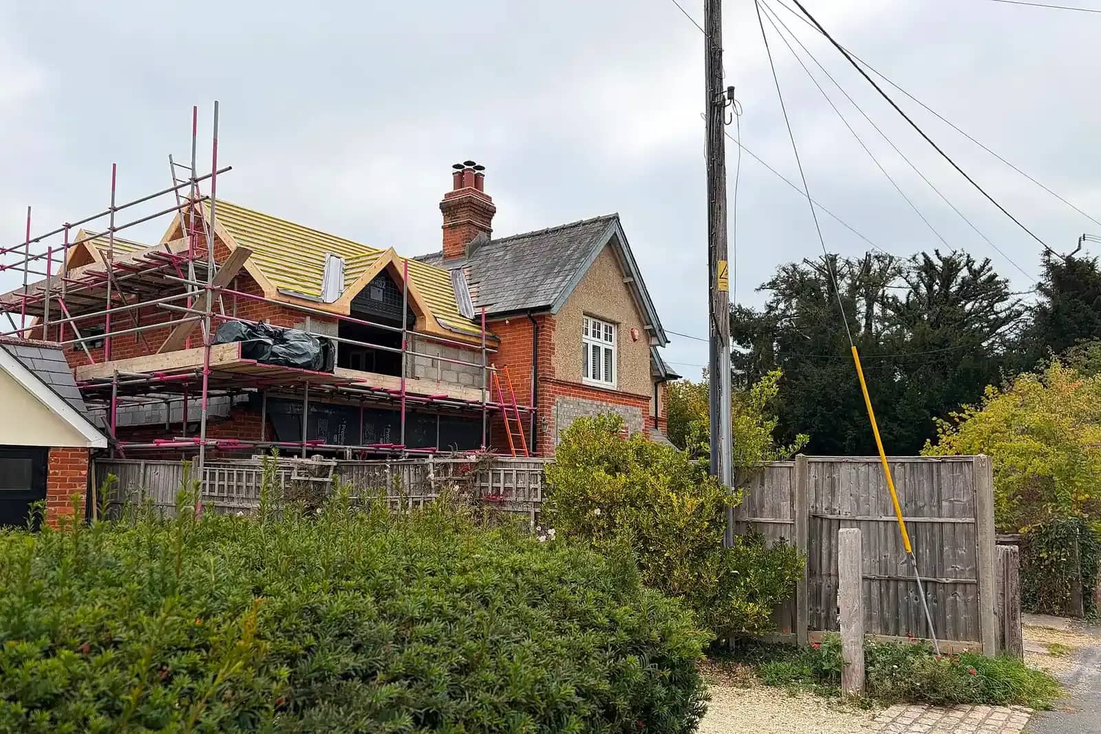 A brick house with a new first-floor roof structure under construction, scaffolding around it and yellow roof membrane on the new frame
