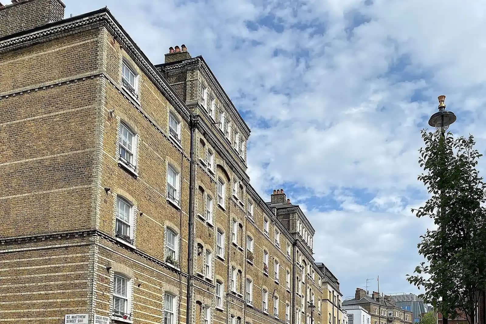 Tall yellow-brick Victorian mansion block on Great Peter Street in Westminster under a blue sky with clouds, a street lamp on the right